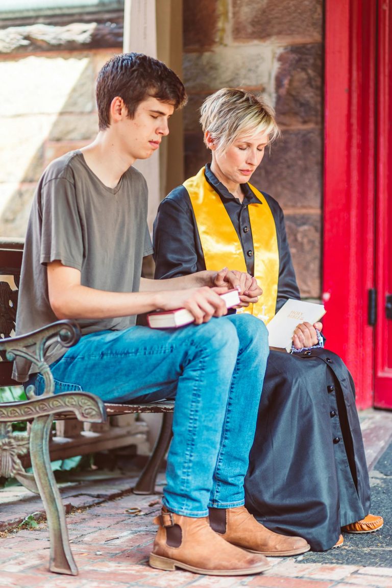 A young man and pastor sit together outdoors, sharing a thoughtful moment.